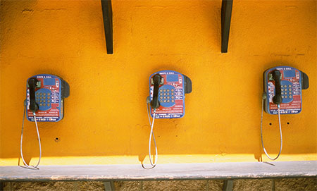 image of vintage telephones lined up on a yellow wall