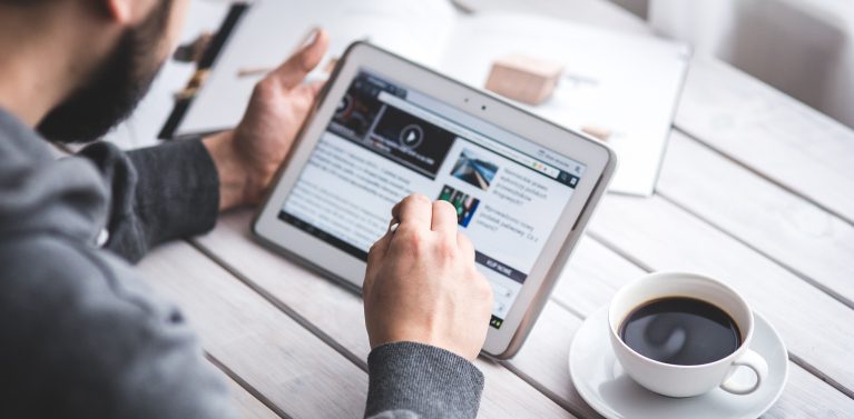 image of a man using an iPad at a white wooden table with a coffee