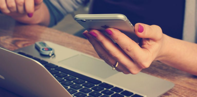 image of a hand holding a phone and a laptop on a wooden table