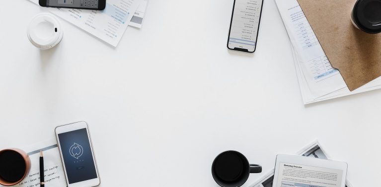 image of papers and phones and stationary on a white table.