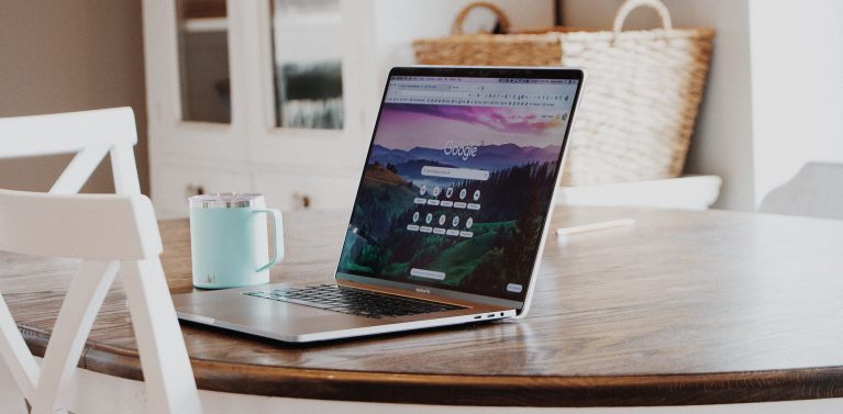 image of google search page open on a laptop, a wooden table with a blue thermal mug in a kitchen dining area.
