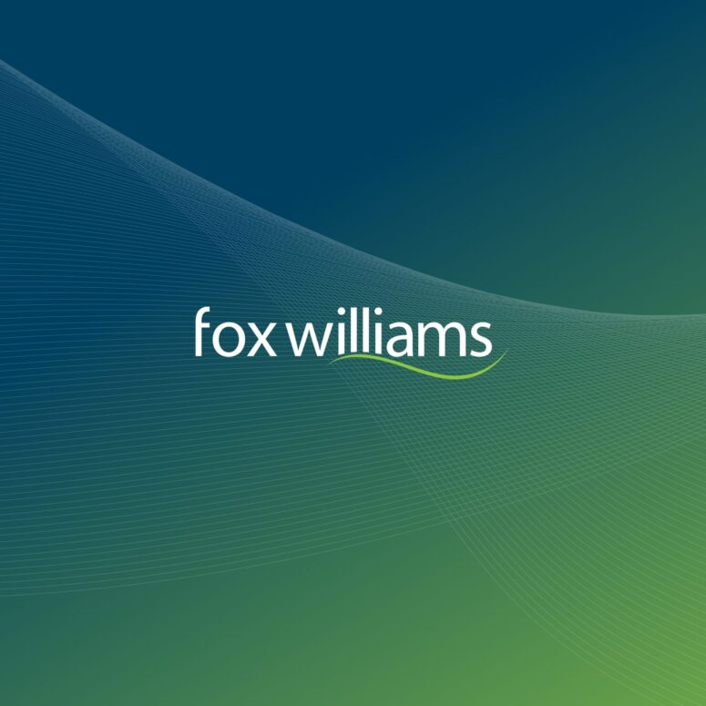 This image shows the logo of "fox williams" displayed in white text in the centre of the image. The logo features a subtle green swoosh under the name. The background is a gradient that transitions from deep blue at the top to green at the bottom.