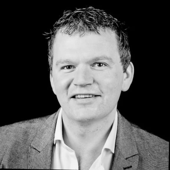 A black and white headshot of Tim in a shirt and blazer
