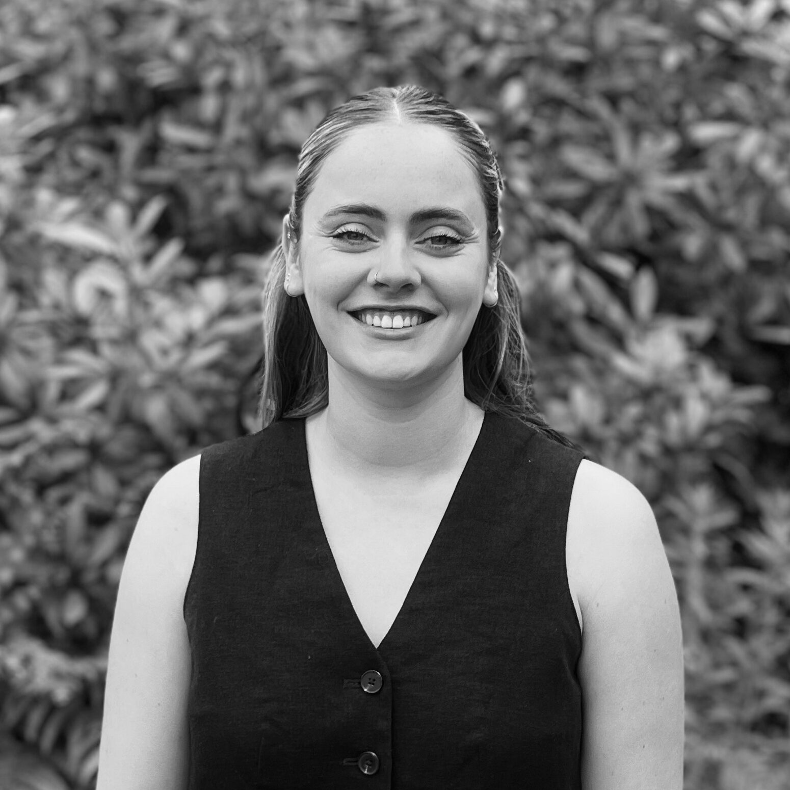 A black and white image of Katie standing in front of foliage