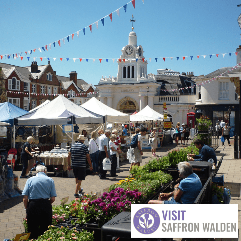 Visit Saffron Walden website image. A photo of Saffron Walden on a summers day with lots of markets stalls and shoppers